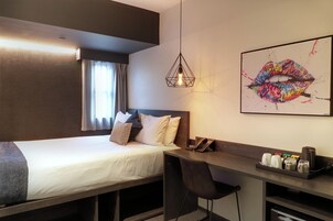A hotel room with a bed, a desk, a chair, a phone, and a coffee machine.