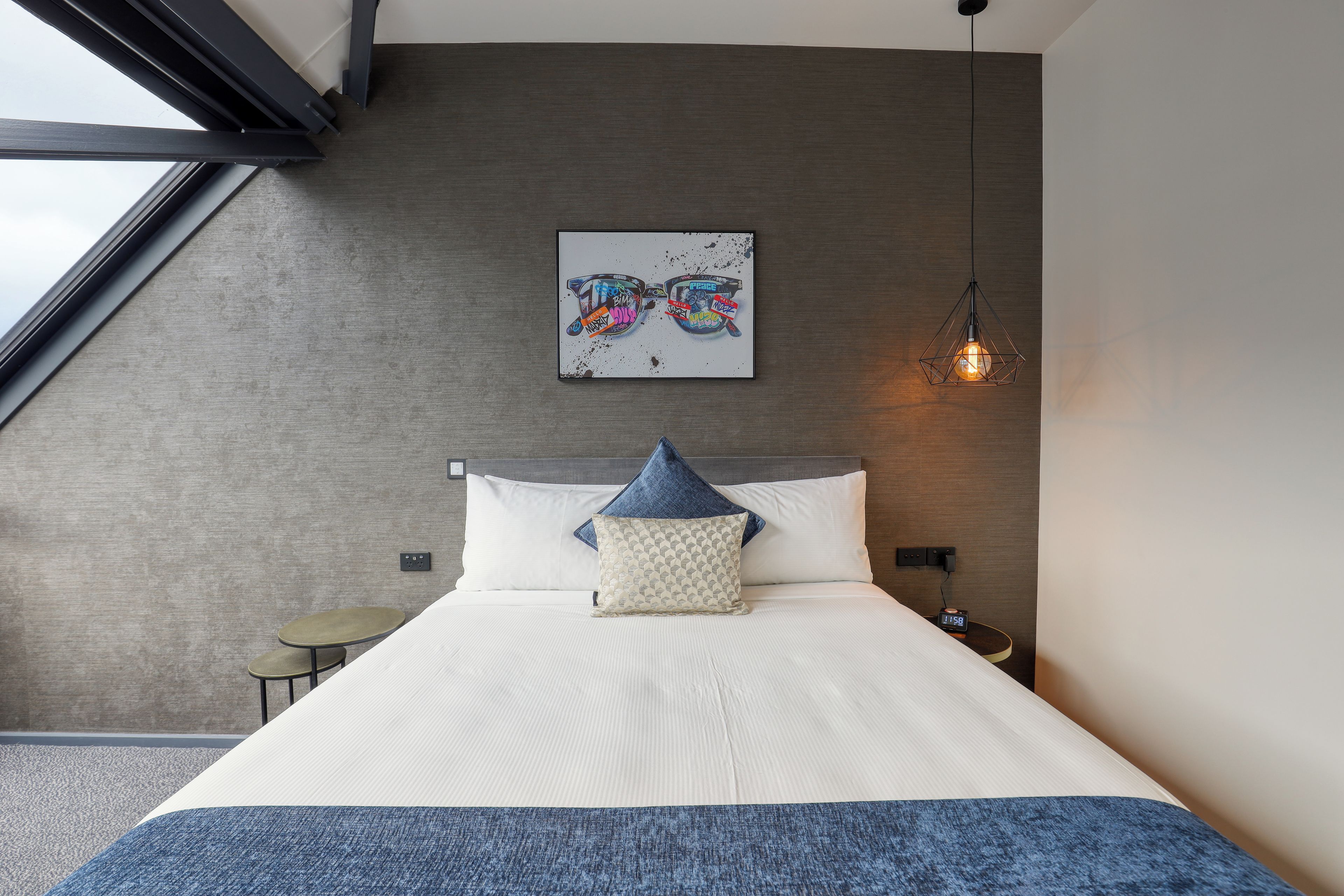 Un dormitorio moderno con una cama grande, una obra de arte en la pared, una lámpara colgante y una mesita de noche pequeña.