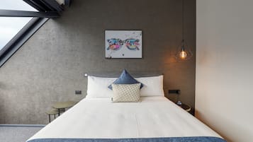 Une chambre à coucher moderne avec un grand lit, une œuvre d’art accrochée au mur, un luminaire suspendu et une petite table de chevet.