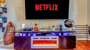 En moderne stue med et stort fjernsyn, der viser "NETFLIX", en træstol formet som en fisk, en globus og en pejs.