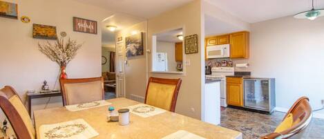 A dining area with a table set for four, a kitchen with wooden cabinets, and a refrigerator.
