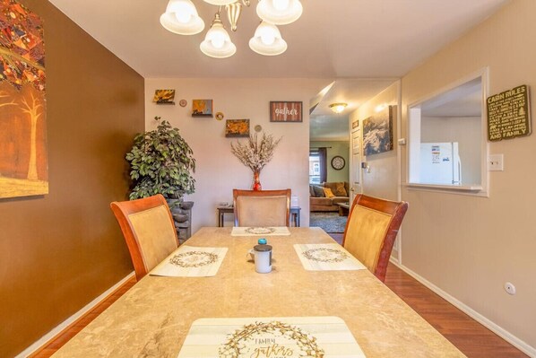 A dining room with a long table, four chairs, a chandelier, and wall decorations.