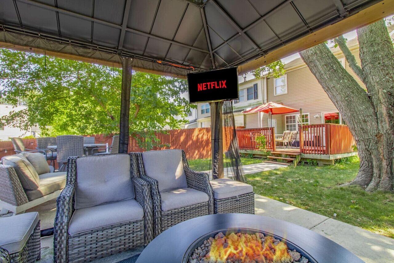 A covered outdoor seating area with wicker furniture, a fire pit, and a sign indicating a Netflix service.