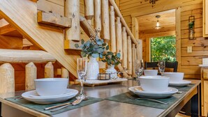 Un interno in legno con un tavolo da pranzo apparecchiato per quattro persone, con piatti, ciotole e bicchieri bianchi.