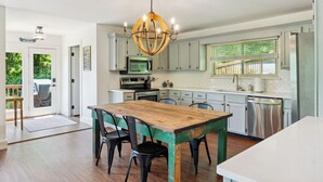Une cuisine avec une table en bois, des chaises, un lustre et des appareils électroménagers modernes.