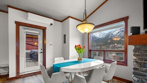 Een eetgedeelte met een ronde tafel, grijze stoelen, een blauwe kleed en uitzicht op bergen door een groot raam.