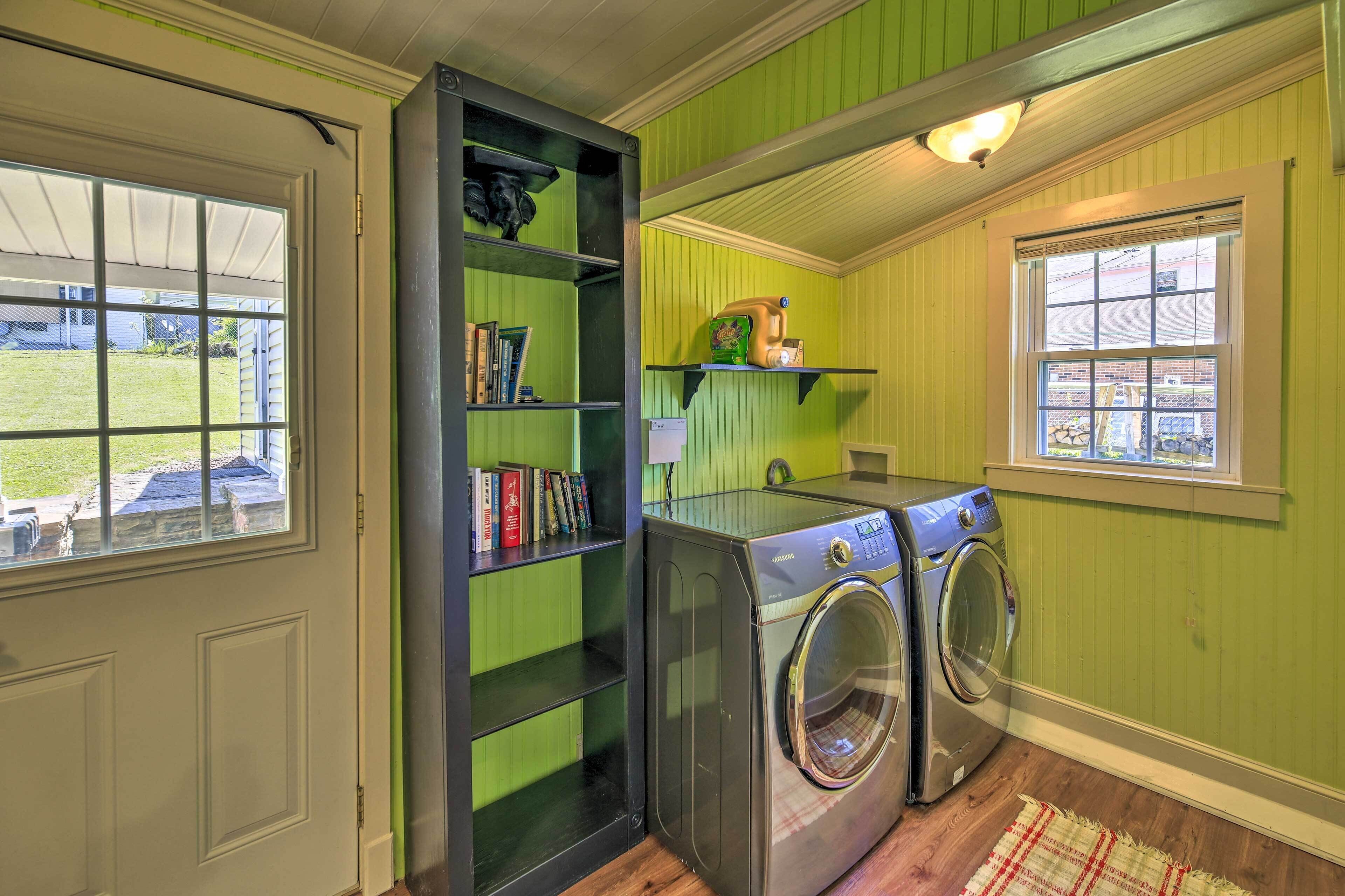 A laundry room with two front-loading washing machines, a shelf with books, and a window with a view of the outside.