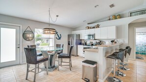 Una cocina moderna con una isla central, taburetes de bar y un comedor con sillas.