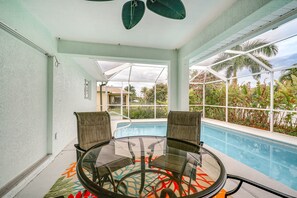 Una mesa de vidrio con dos sillas en una habitación con vista a una piscina y plantas tropicales.