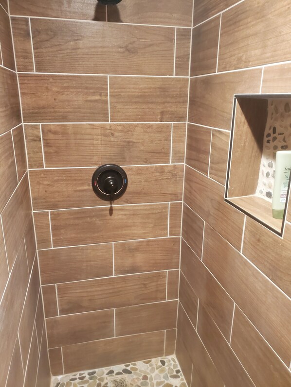 A shower area with wooden tiles and a black showerhead. - Three Forks Saddlery's Stable (Three Forks)