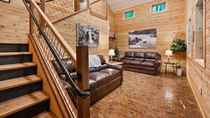 A wooden interior with a staircase, leather sofa, and two paintings.