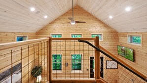 A wooden interior with a sloped ceiling, a ceiling fan, and a staircase with a metal railing.