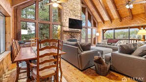 A spacious living area with a stone fireplace, large windows, and wooden furniture.