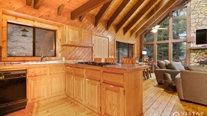 A spacious kitchen with wooden cabinets, a central island, and a stone fireplace.