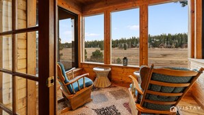 A wooden cabin with large windows, two wooden chairs with cushions, and a small round table.