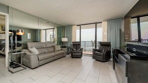 Una sala moderna con un sofá, dos sillones, un televisor y un balcón con cortinas.