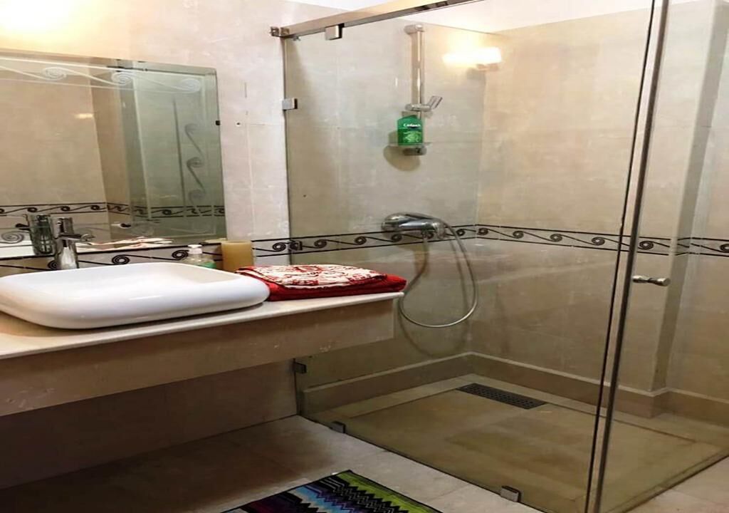 Un baño con ducha de vidrio, un lavabo con espejo y una alfombra estampada en el suelo.