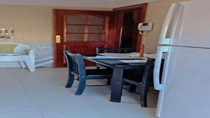 Zona pranzo con tavolo e sedie, un frigorifero e una porta in legno con pannelli di vetro.