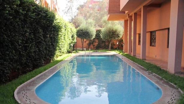 Una piscina rettangolare con bordo piastrellato, circondata da erba e un siepe.