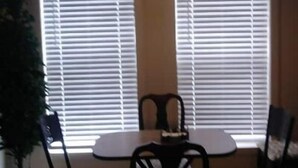 A dining area with a table and chairs, a hanging light fixture, and a window with blinds. - Cute and Cozy (Rockford)