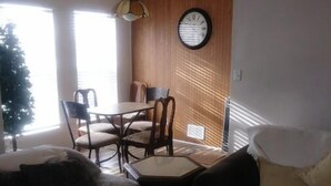 A living room with a sofa, a coffee table, and a dining table with chairs. There is a clock on the wall and a Christmas tree in the corner. - Cute and Cozy (Rockford)