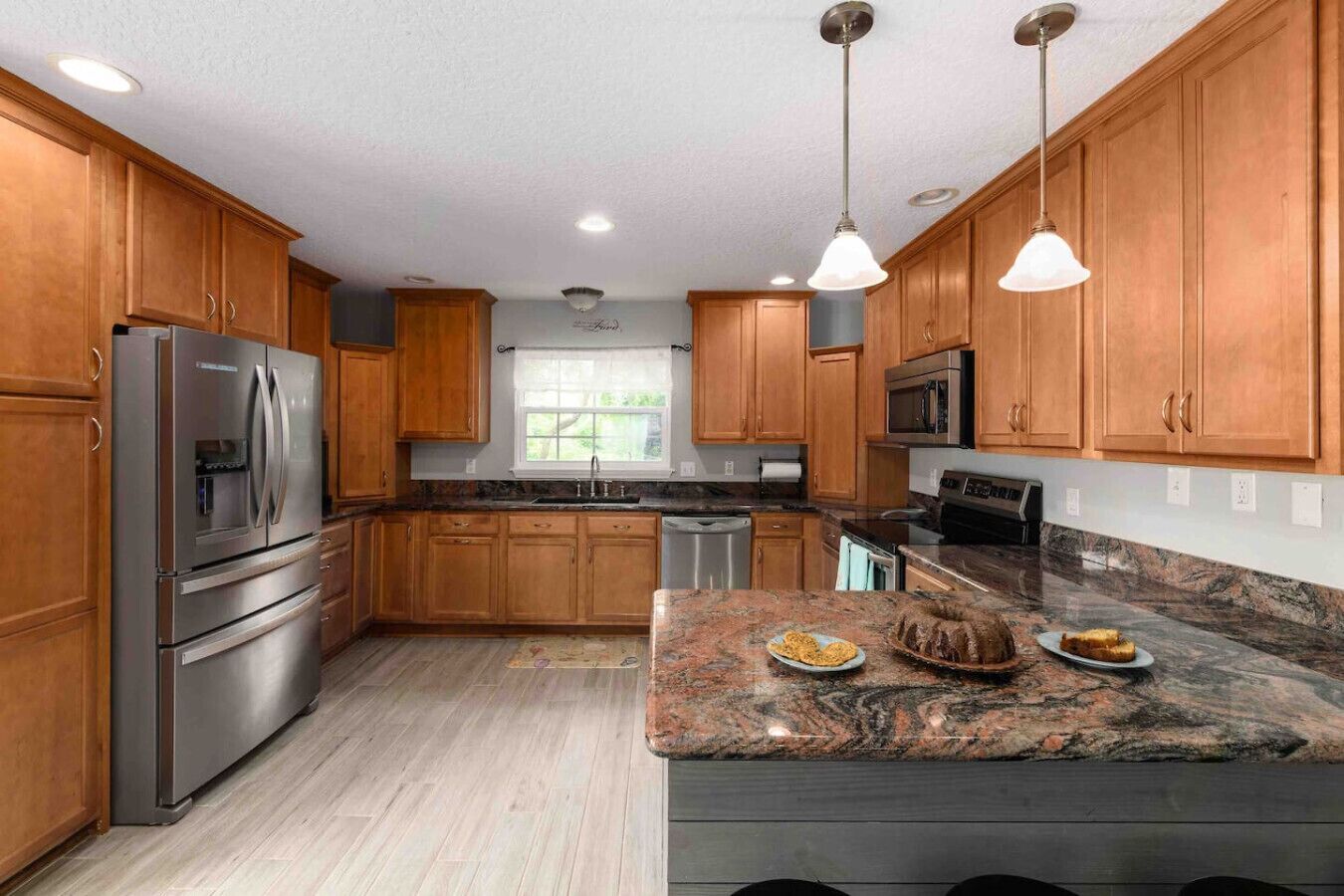 A kitchen with wooden cabinets, stainless steel appliances, granite countertops, and pendant lighting.