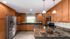 Une cuisine dotée de meubles en bois, d’appareils électroménagers en acier inoxydable, de plans de travail en granit et de luminaires suspendus.