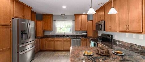A kitchen with wooden cabinets, stainless steel appliances, granite countertops, and pendant lighting.