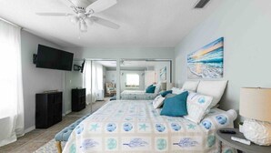 Une chambre d’hôtel avec un lit, une télévision, un ventilateur de plafond, un tableau et une vue sur la plage.