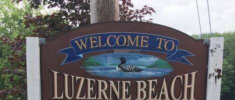 En välkomstskylt för Luzerne Beach med information om badregler och maximalt antal besökare: 100.
