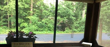 A dining area with a table and chairs, a window with blinds, and a view of greenery outside.