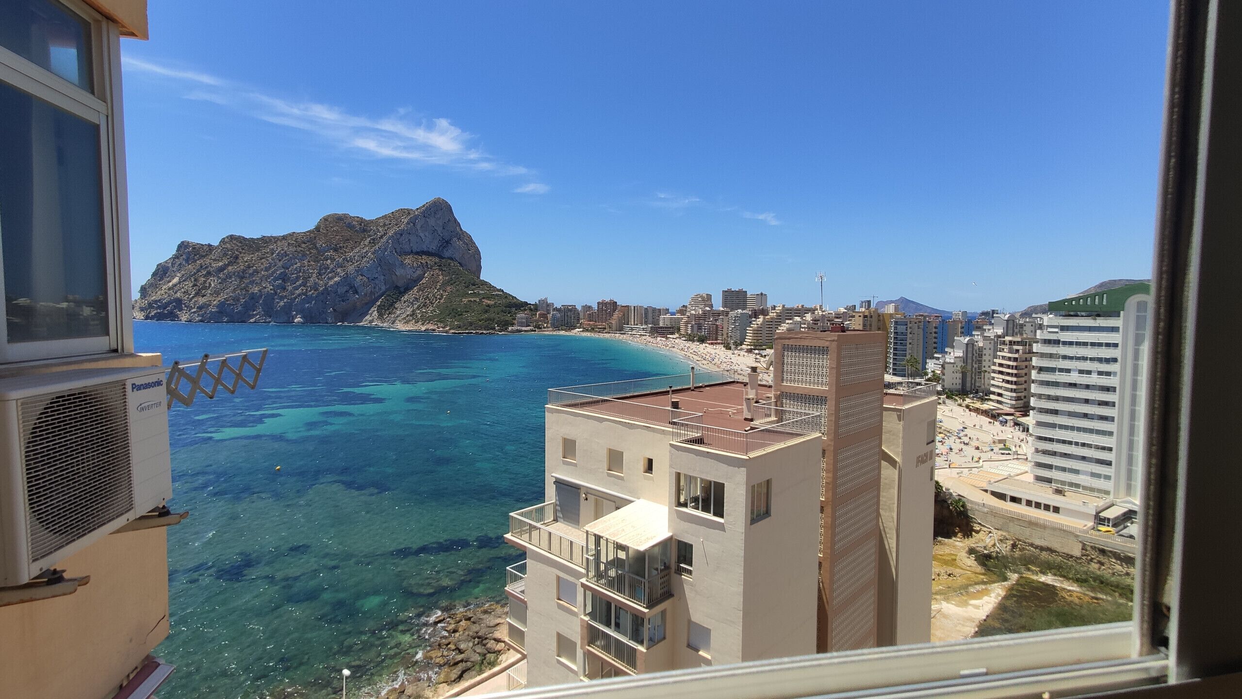 A coastal cityscape with clear blue waters, a rocky mountain, and modern buildings.