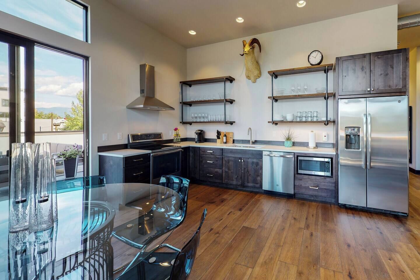 A modern kitchen with a glass dining table, stainless steel appliances, and a mounted animal head.