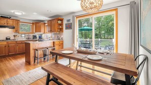 Una cocina con armarios de madera, una mesa de comedor con bancos y un amplio ventanal con vistas al exterior.