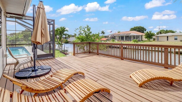 Eine Holzterrasse mit Liegestühlen und Billardtisch, mit Blick auf ein Gewässer und eine Wohngegend.