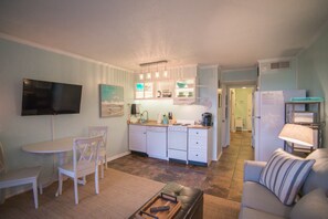 Un espacio habitable compacto con comedor, kitchenette y zona de estar con sofá y mesa de centro.