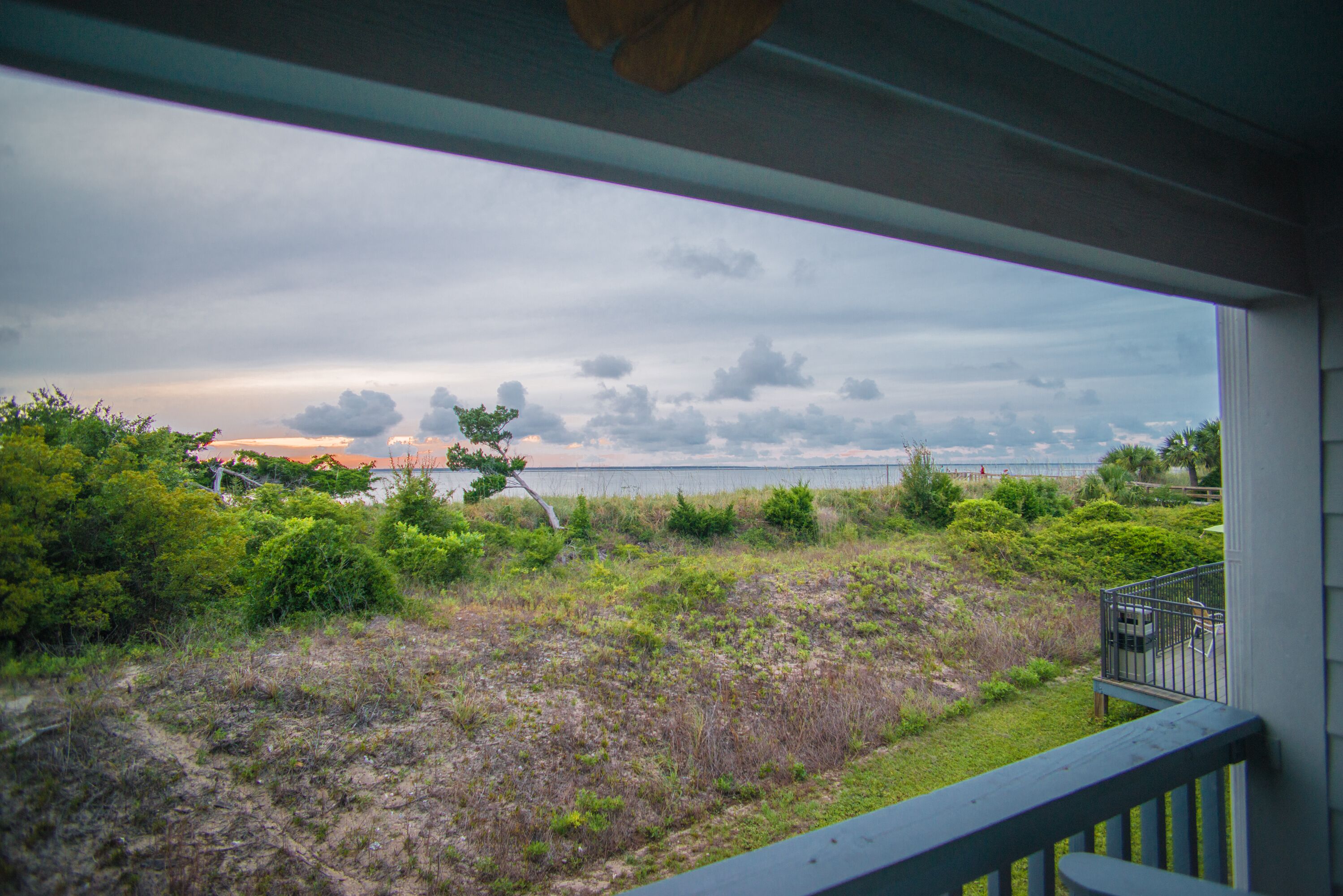 A view from a balcony overlooking a grassy area with a body of water and a cloudy sky.