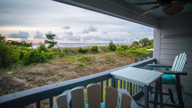 Un balcone con vista sulla spiaggia, un tavolo, due sedie e una ventola a soffitto.