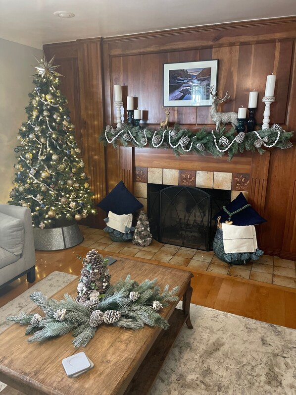 A cozy living room with a decorated Christmas tree, a fireplace mantel with candles, and a small Christmas tree on a table. - NEW HOT TUB||sleeps 10|4BR 3Ba|firepit|pingpong table|New River Gorge NP (Fayetteville)