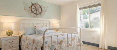 Un dormitorio con cama, mesitas de noche, un adorno en la pared y una ventana con cortinas.