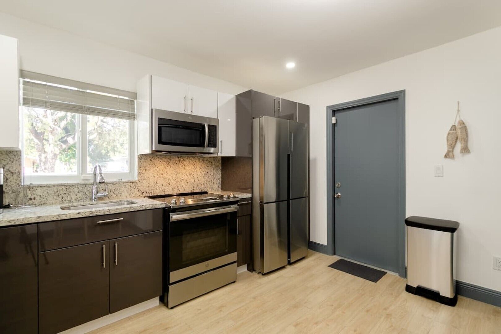 A modern kitchen with stainless steel appliances, a granite countertop, and a window with blinds.