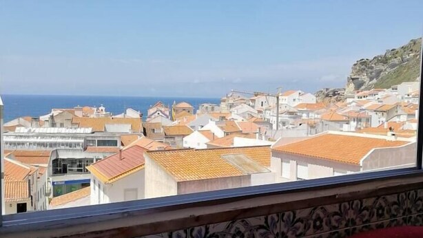 A table with a green drink, white flowers, and a view of a coastal town with terracotta roofs.