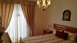 A bedroom with a bed, a nightstand, a lamp, a painting on the wall, and a window with curtains.