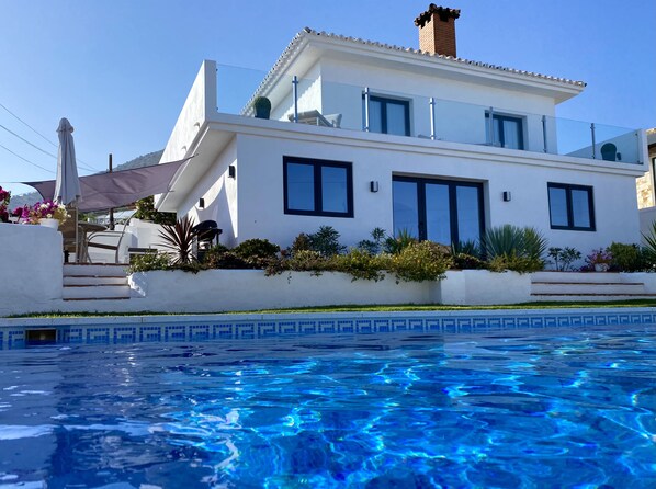 A modern two-story house with a swimming pool in the foreground.