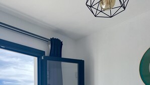 Ein Schlafzimmer mit einem Bett, einem Nachttisch, einer Wandleuchte und Blick auf das Meer durch eine Glastür.