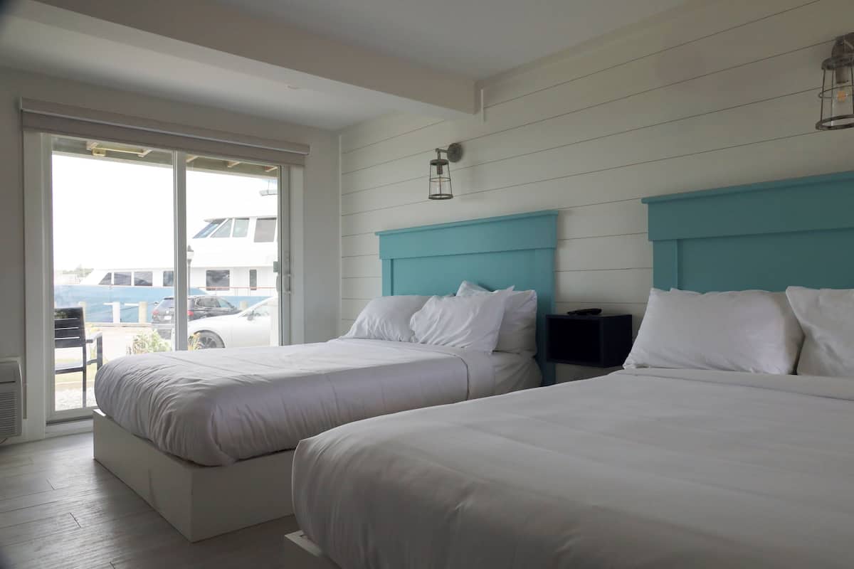 Habitación de hotel con dos camas, una puerta corrediza de vidrio al exterior y un cabecero color aguamarina.