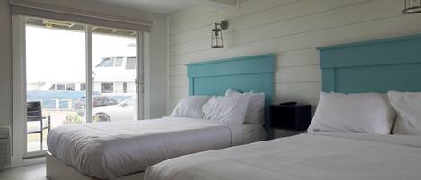 Habitación de hotel con dos camas, una puerta corrediza de vidrio al exterior y un cabecero color aguamarina.