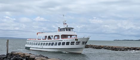 A white boat named 'Island Queen' docked at a rocky pier with a view of the sea and distant land.