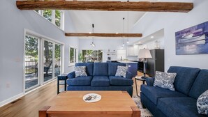 A spacious living room with a blue sofa set, wooden coffee table, and large windows offering a view of the outdoors. - Pearl Beach:  Dive into Summer Fun at Pearl Beach – Swim, Kayak & Relax! (Greenville)