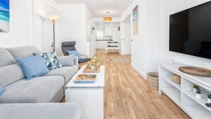 A modern living room with a grey sofa, a coffee table, a TV, and a kitchen in the background. - Lola Playa by Interhome (Benalmádena Costa)